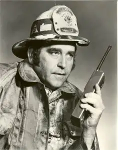 A firefighter in uniform holds a radio, looking to the side, ready to respond—highlighting the spirit of innovation at the heart of About the Innovation Hub.