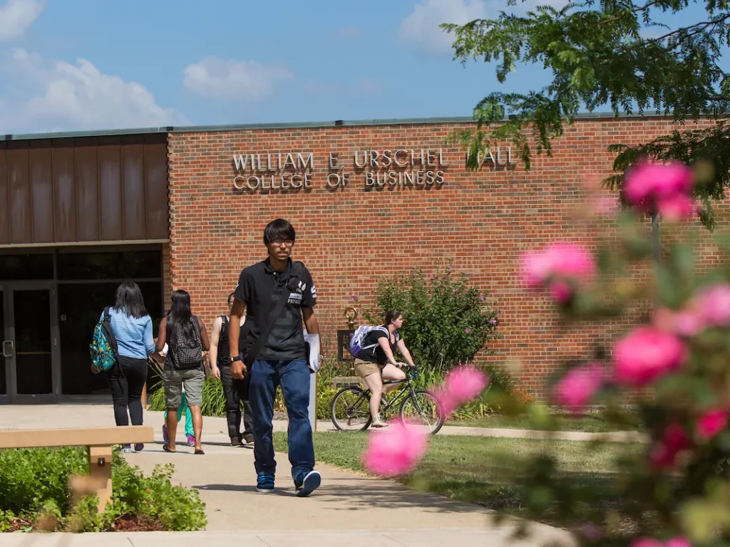 Students walk and bike outside William E. Urschel Hall, home to the College of Business and its Accounting program, with flowers in the foreground.