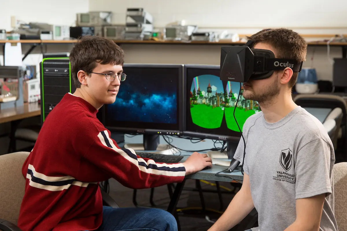 Two young men explore a virtual reality headset and computer in a technology lab, highlighting the innovative world of computer engineering.