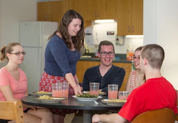 Four young adults sit around a table, sharing a meal and drinks in a casual kitchen setting, enjoying good food and conversation focused on Health & Wellness.