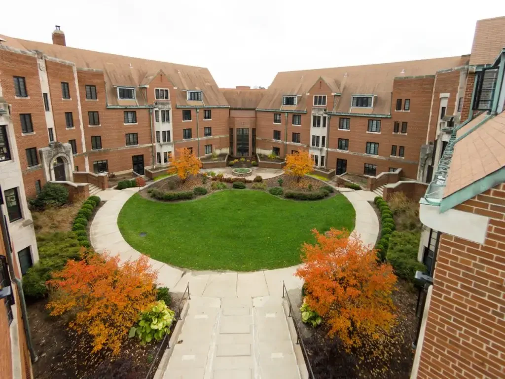 Guild-Memorial Hall is a brick dormitory building that surrounds a circular grassy courtyard with autumn trees and winding pathways.