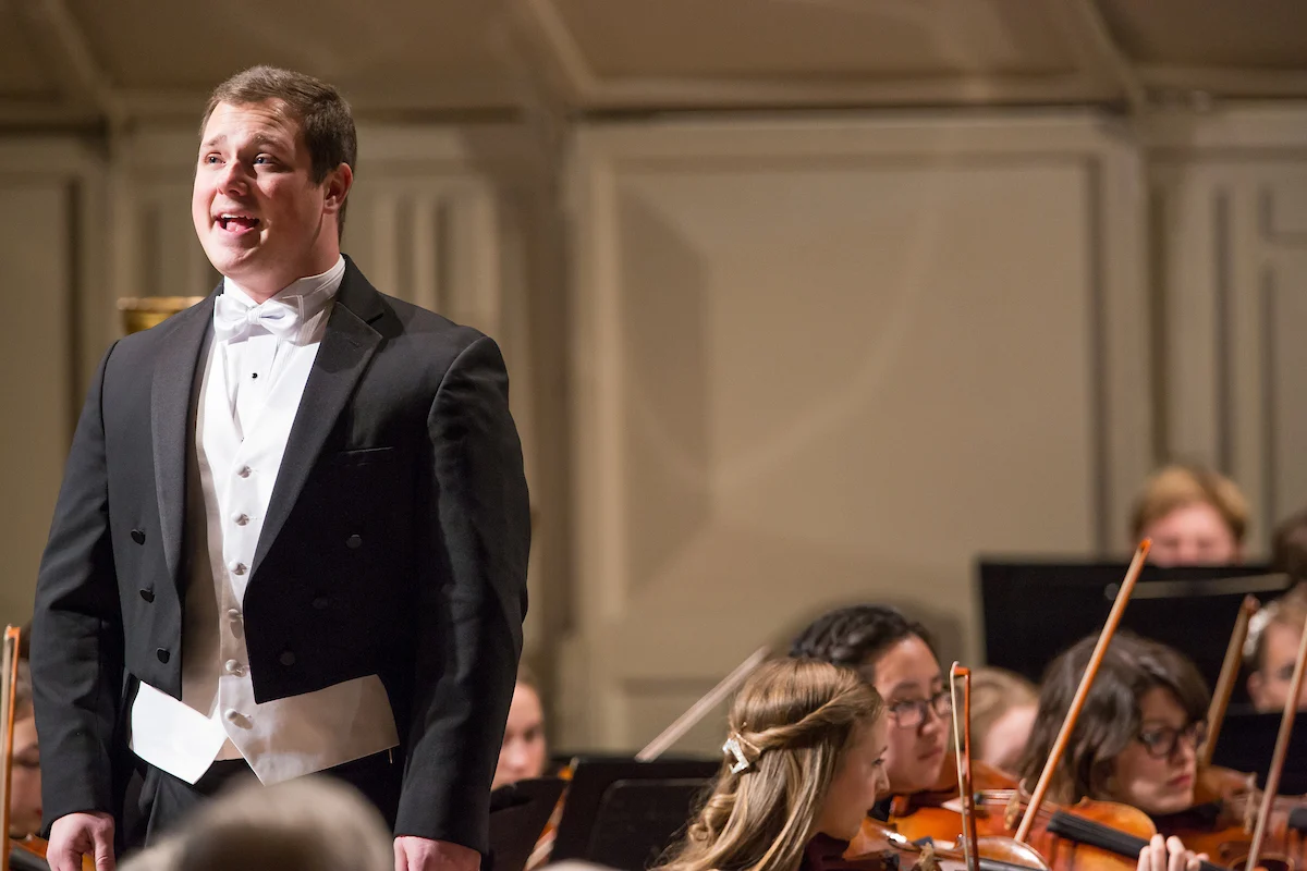 A man in a tuxedo sings on stage with an orchestra playing behind him, creating a magical evening that embodies the spirit of Uplift Valpo.