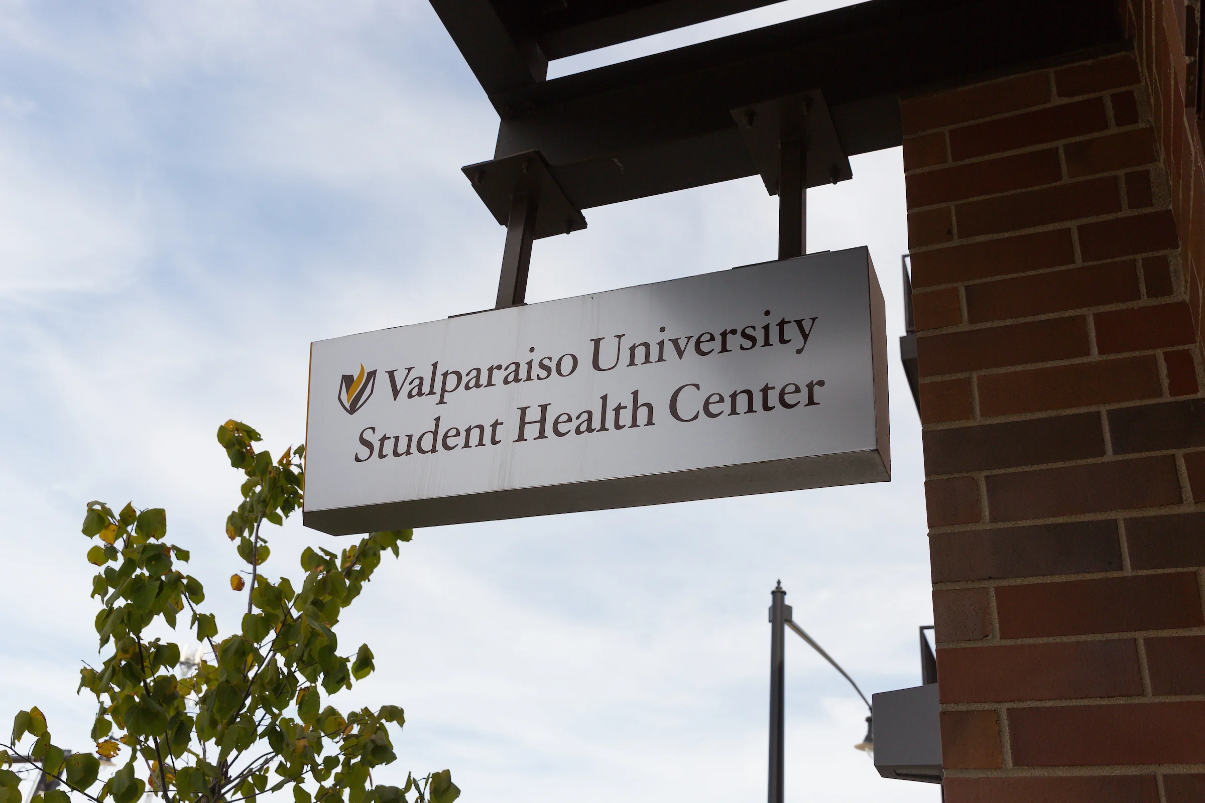 Sign for Valparaiso University Student Health and Wellness Center, mounted on a brick building with the sky in the background.