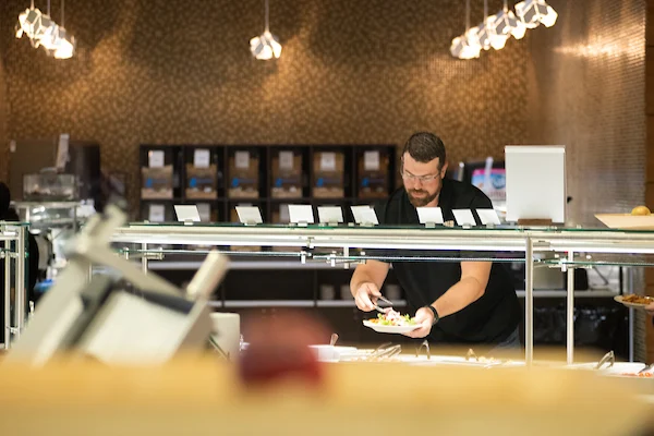 A man serves himself food at a buffet counter in a well-lit, modern dining area focused on health & wellness.