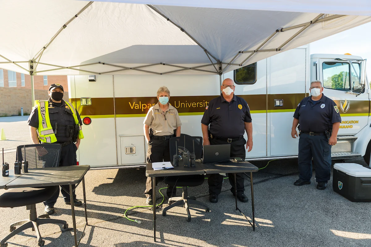 Four uniformed people wearing masks stand in front of a Valparaiso University emergency vehicle and tent on campus.