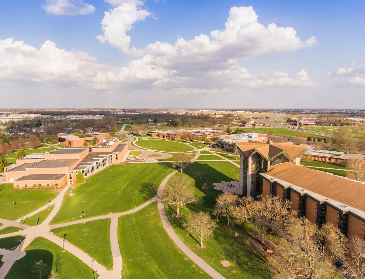 Aerial view of a college campus with green lawns, paths, and several modern brick buildings under a partly cloudy sky, home to VCUCR (Valparaiso University Office for Civil Rights).