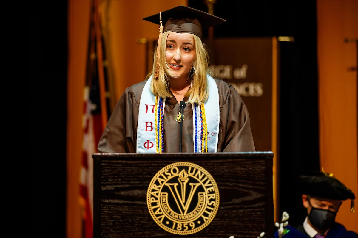 A graduate in cap and gown speaks at a podium during a university graduation ceremony, sharing important Information for Graduates.