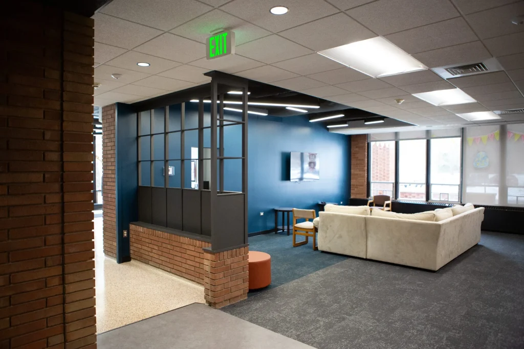 Modern lounge area with white couches, blue walls, and large windows letting in natural light.