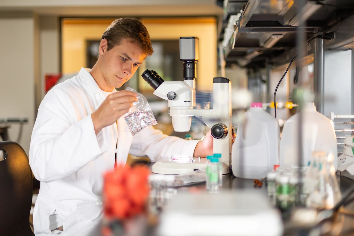 A scientist in a lab coat examines a sample in front of a microscope, illustrating the hands-on learning approach often found in a Peer Tutoring Program within laboratory settings.