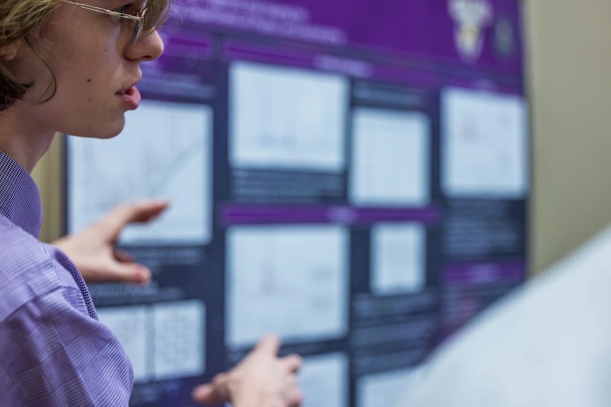 A member of the Committee to Enhance Learning & Teaching presents a scientific poster, showcasing charts and graphs in the background.