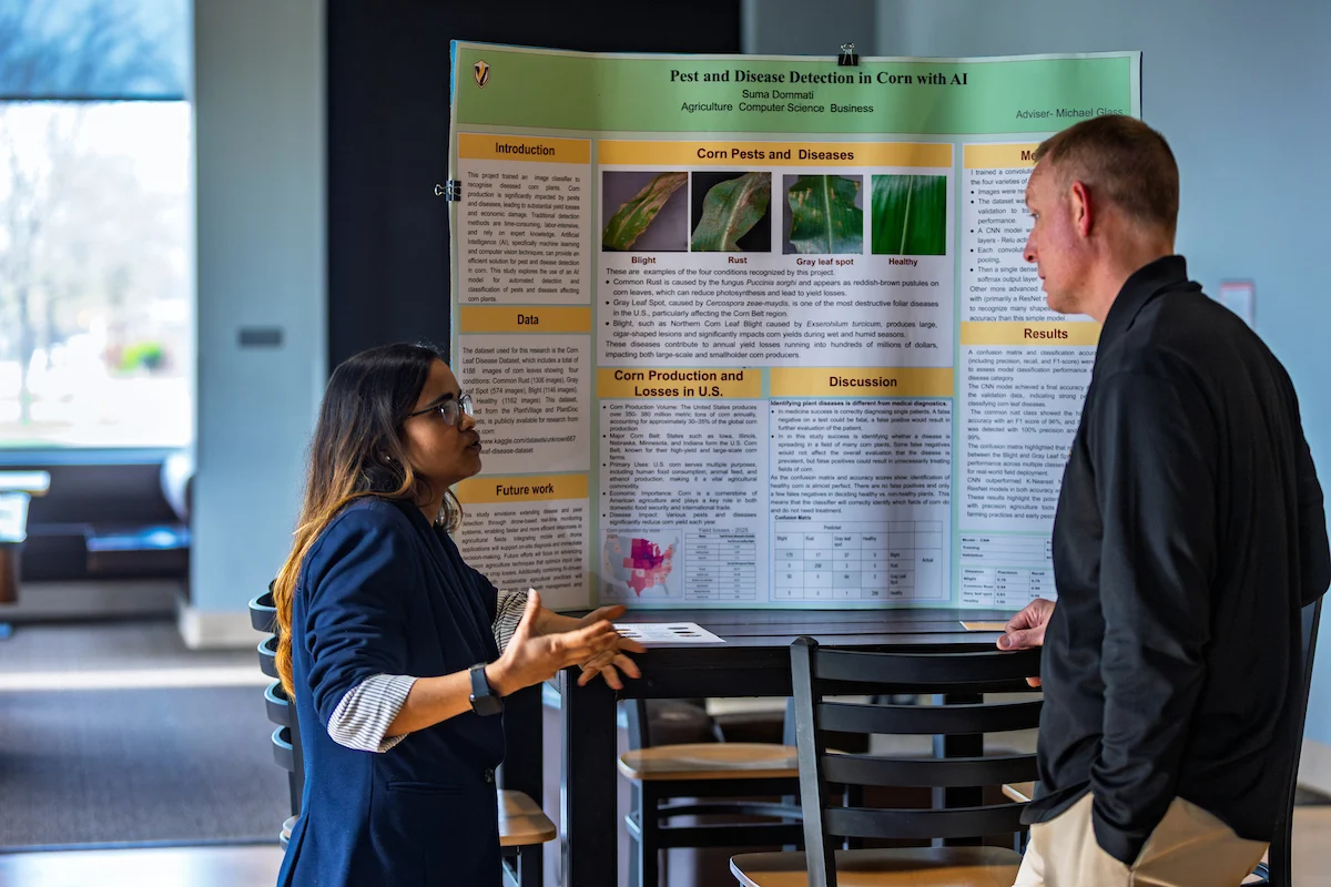 Two people from the Committee to Enhance Learning & Teaching discuss a science fair project display about pest and disease detection in corn with AI.
