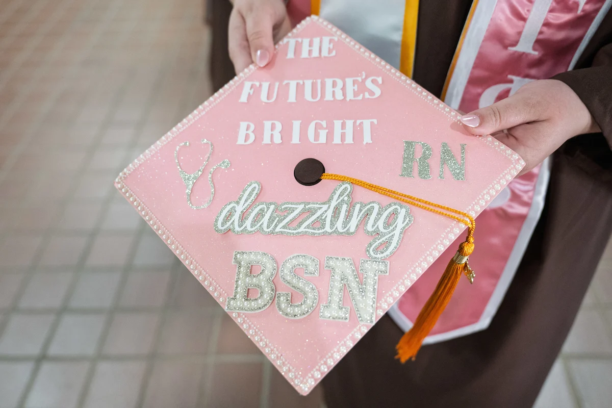 Person holding a pink graduation cap decorated with “The Future’s Bright, dazzling BSN, RN” in glittery letters, celebrating their achievement with support from EdAssist.
