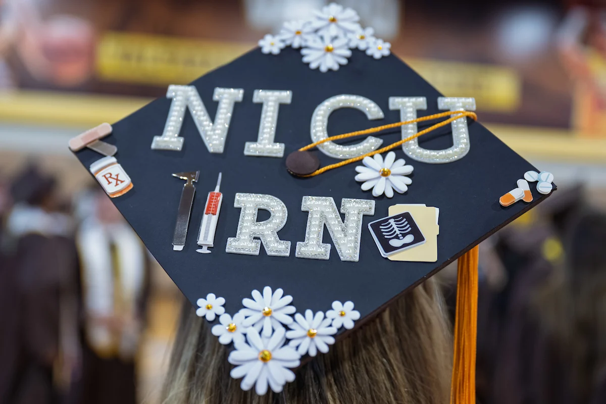 Graduation cap decorated with flowers and letters spelling "NICU RN," medical-themed stickers, and a nod to EdAssist support.