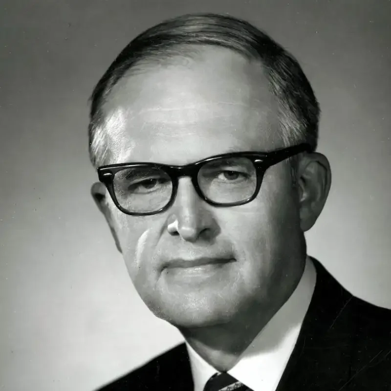 Black and white portrait of an older man wearing glasses and a suit, looking slightly to the side, embodying leadership and governance.