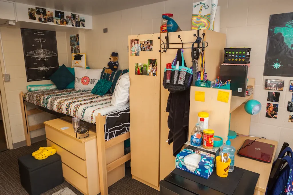 A tidy dorm room with a lofted bed, wooden furniture, photos on walls, and organized personal items.
