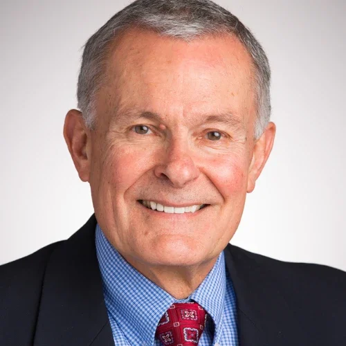 Smiling older man in a suit and tie with short gray hair stands against a plain background, embodying the warmth and values of Our Lutheran Identity.