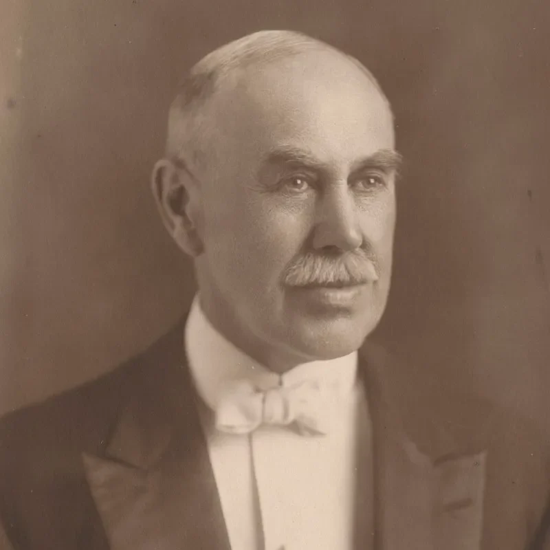Portrait of an older man with a mustache, wearing a suit and bow tie, captured in sepia tones, embodying leadership & governance.