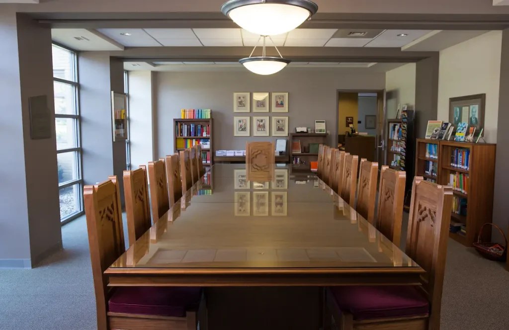 A long wooden conference table with chairs in the Kade-Duesenberg German House library room, surrounded by bookshelves and framed pictures.