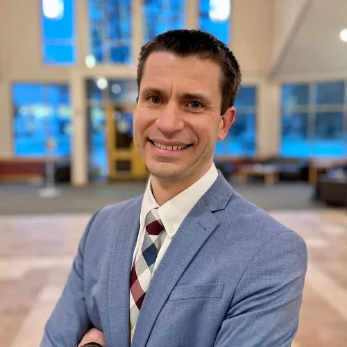 Smiling man in a blue suit and patterned tie standing indoors with blurred background, reflecting our Lutheran Identity.
