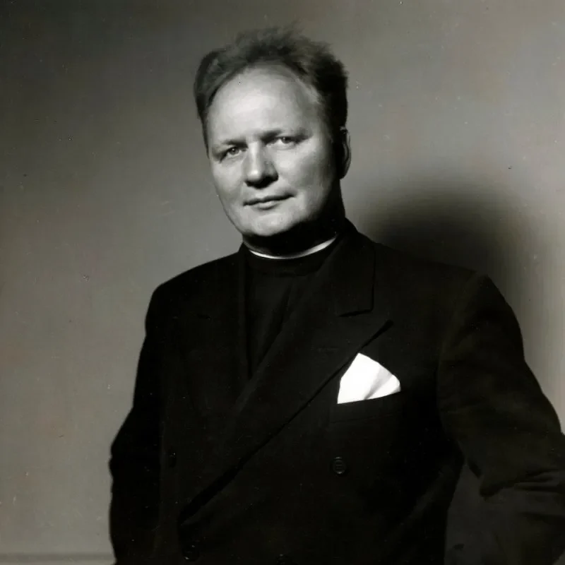 A man in a dark suit with a white pocket square, standing and facing the camera with a neutral expression, radiates an air of leadership and governance.