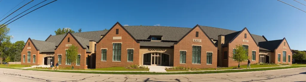 Wide-angle view of a modern, brick sorority housing complex with peaked roofs under a clear blue sky.