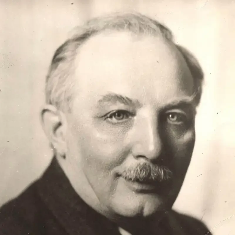 Black-and-white portrait of an older man with a mustache, wearing a dark jacket, facing the camera—his expression reflects wisdom and experience in leadership & governance.