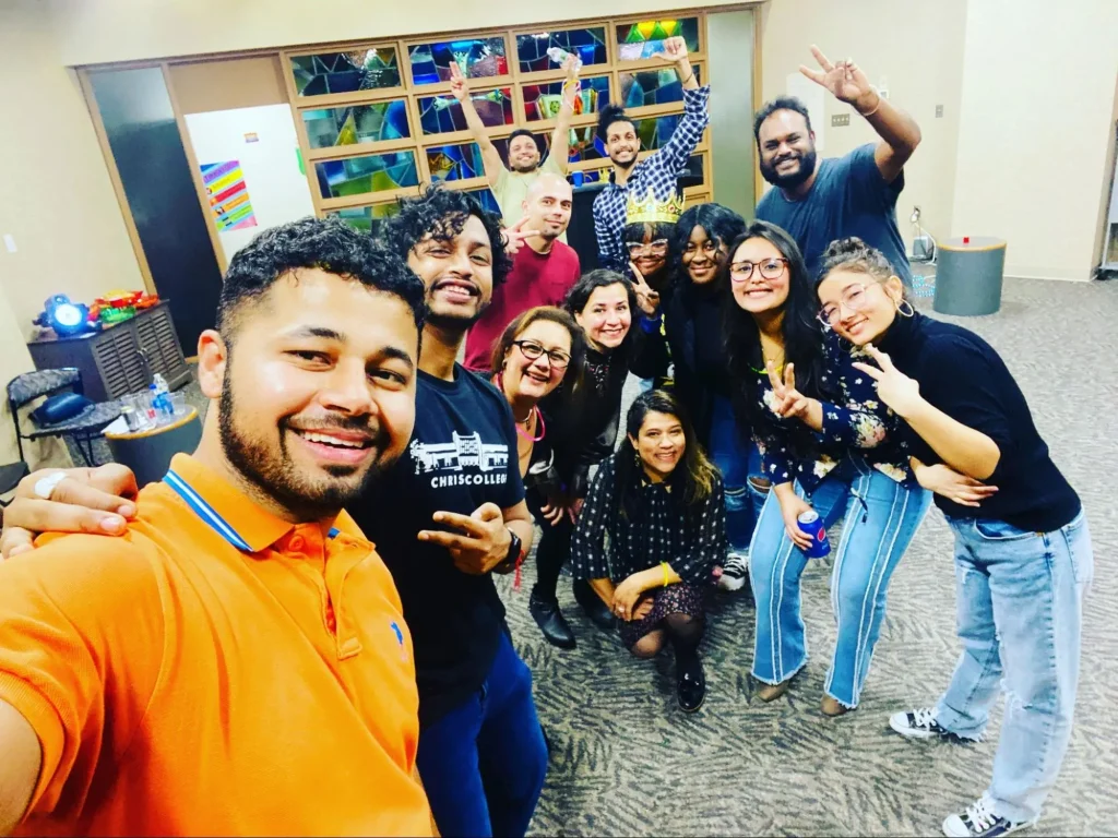 A group of people smiling and posing for a Vale selfie indoors, making peace signs and cheerful expressions.