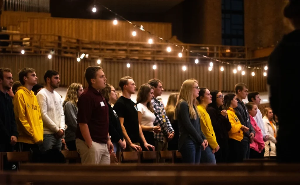 A group of people stand together indoors under string lights in Vale, appearing attentive and engaged.