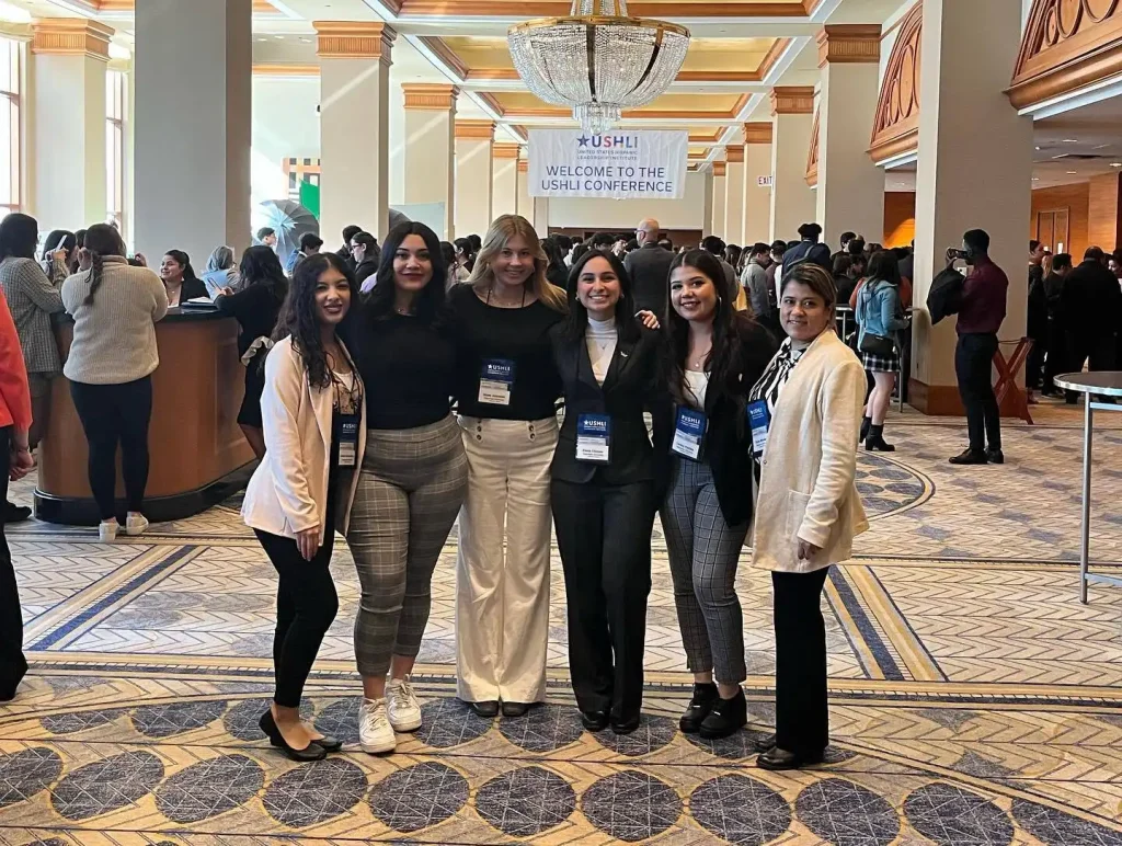 Six women, including Vale, pose together at a conference with a USHLI Conference welcome sign in the background.