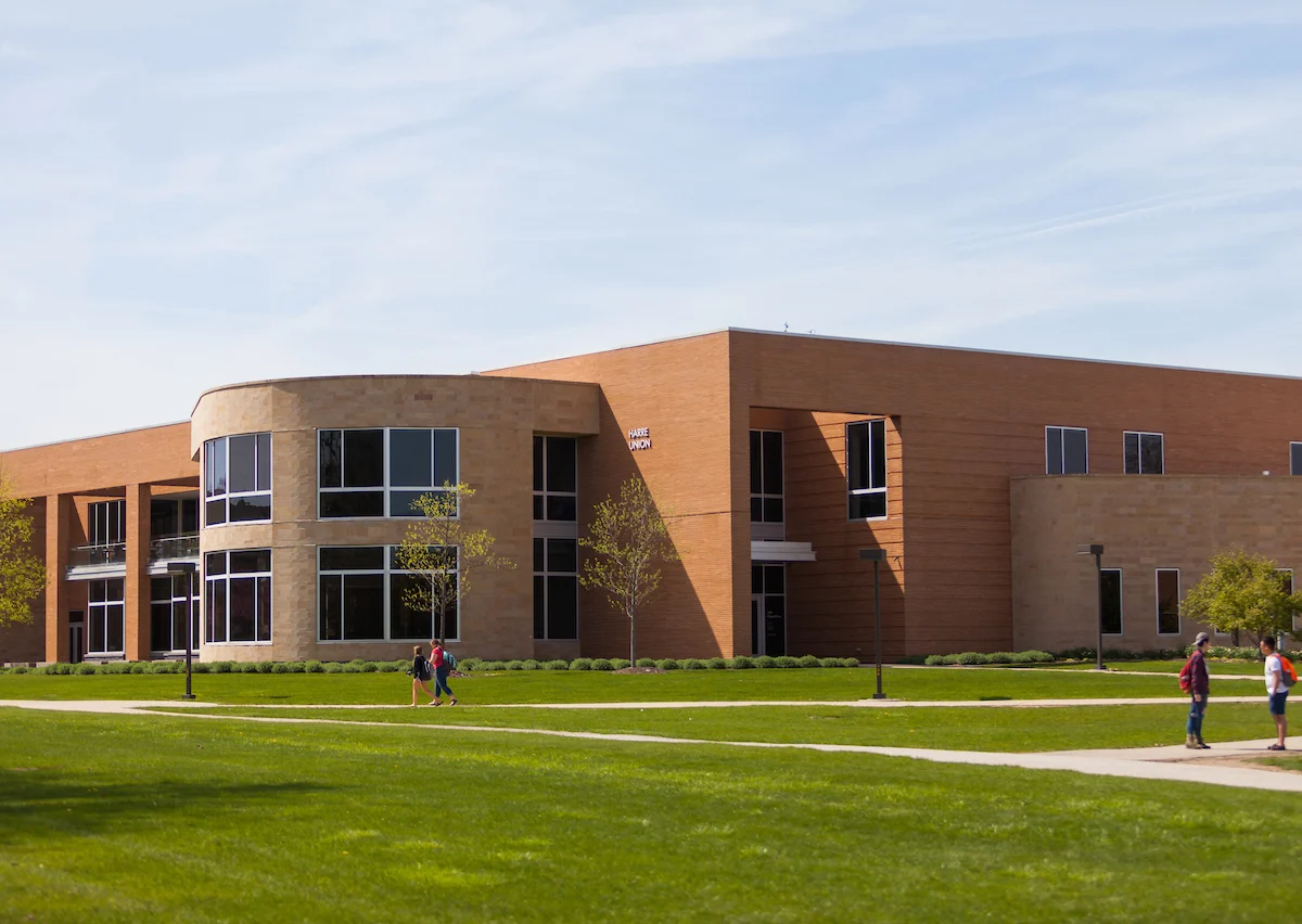 Modern school building with large windows, surrounded by a green lawn, and a few students walking outside—easy to find with Maps & Directions.
