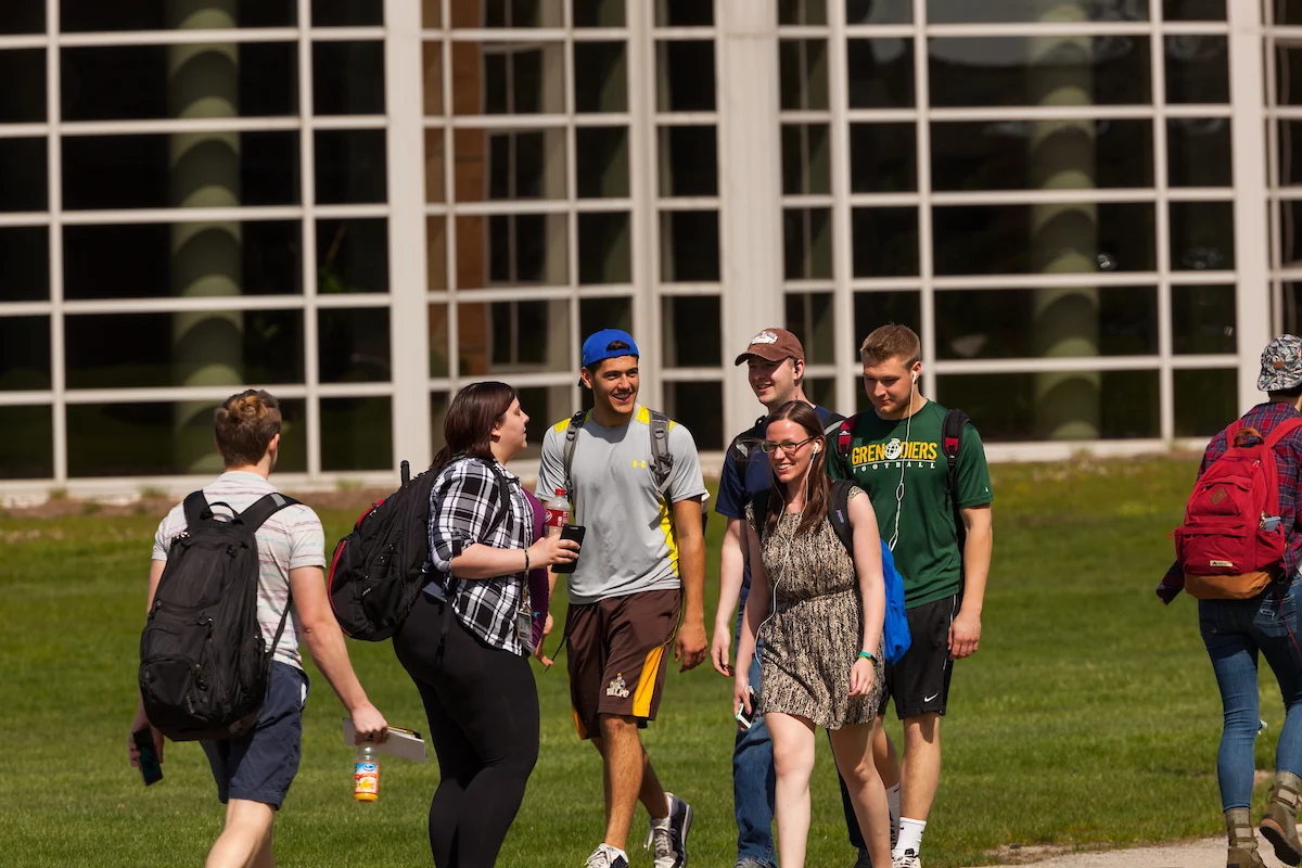 A group of college students walk and talk outside a building with large glass windows, discussing their recent assessment.