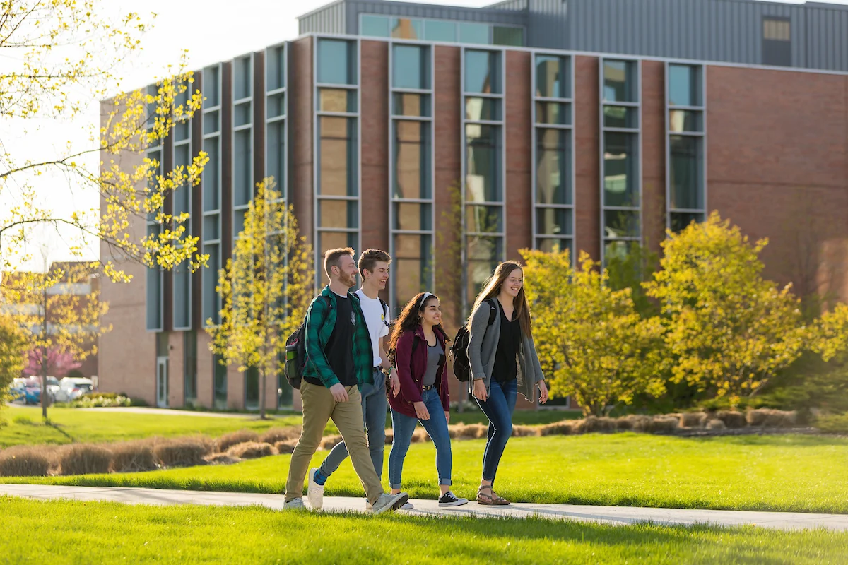 Four students walk together on a sunny day in front of a modern campus building near the Residence Halls.