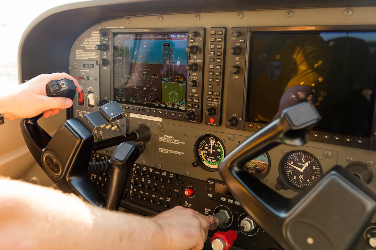 Hands on airplane controls in a cockpit, with digital and analog flight instruments visible—perfect for those passionate about travel and parking their aircraft with precision.