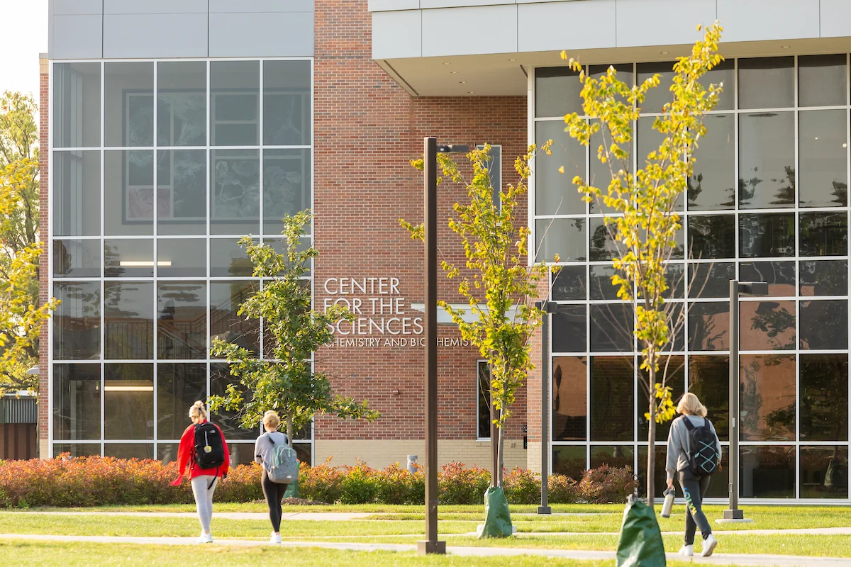 Three students walk outside the Center for the Sciences building on a sunny day, discussing their Critical Threat Response coursework.