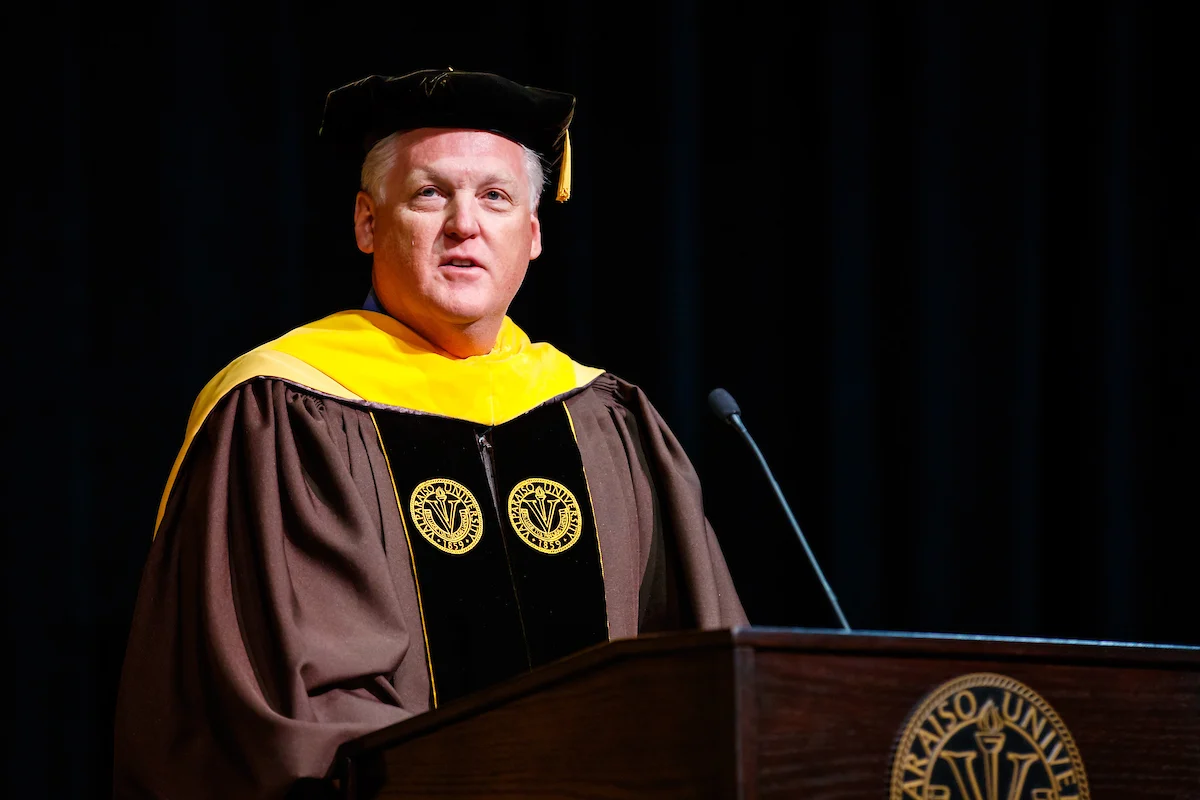 A person in academic regalia speaks at a podium during a graduation ceremony, highlighting the importance of transcript services for graduates as they pursue further education and career opportunities.