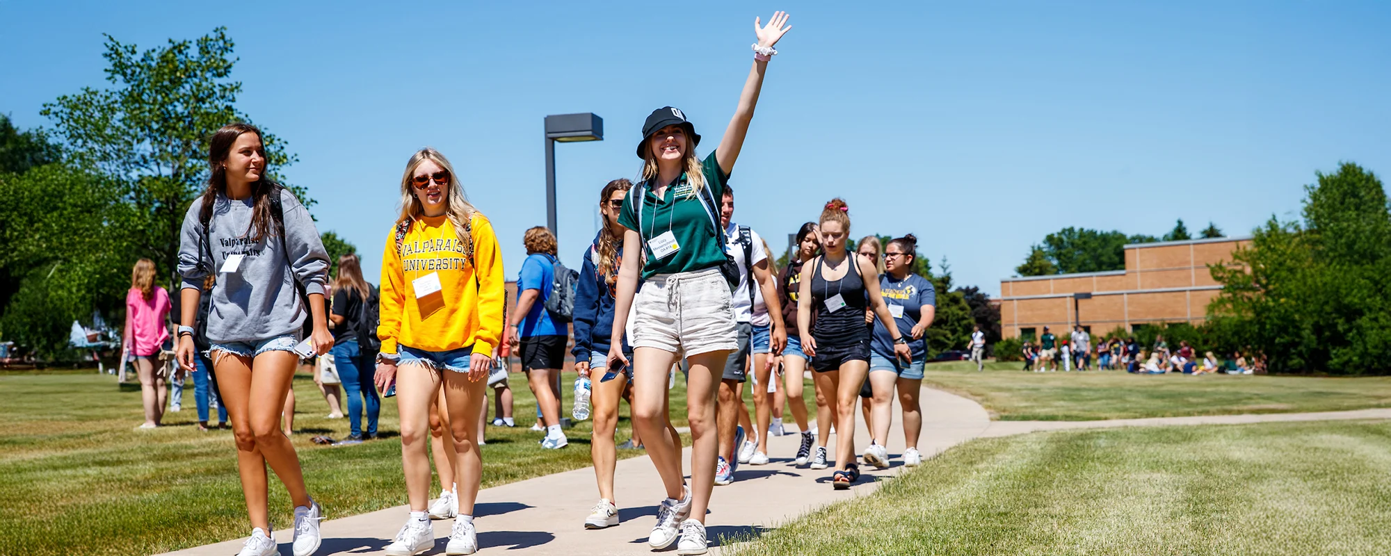 A group of smiling students walk outside on a sunny day, one waving with excitement as they discuss their new Focus Schedules.