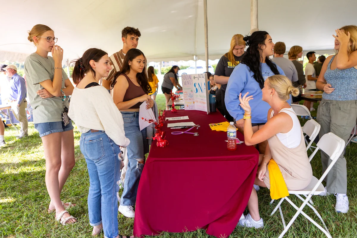 Students gather around a table with flyers at an outdoor event under a large white tent, showcasing opportunities for Student Involvement.