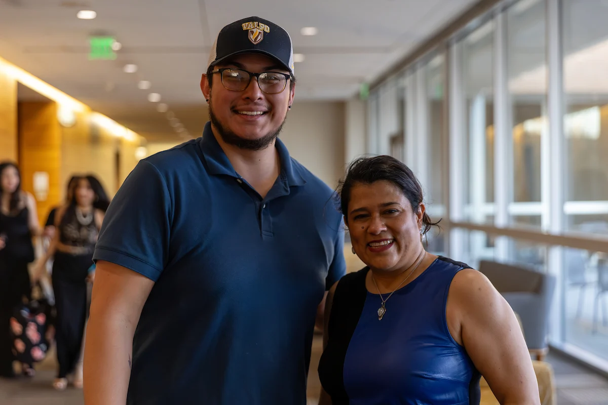 A smiling man in a cap and glasses stands beside a smiling woman in a blue sleeveless top indoors, reflecting the spirit of Multicultural Resources.