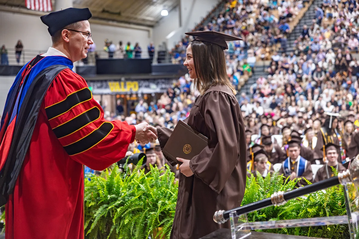 A graduate in cap and gown shakes hands with a faculty member during a lively commencement ceremony.