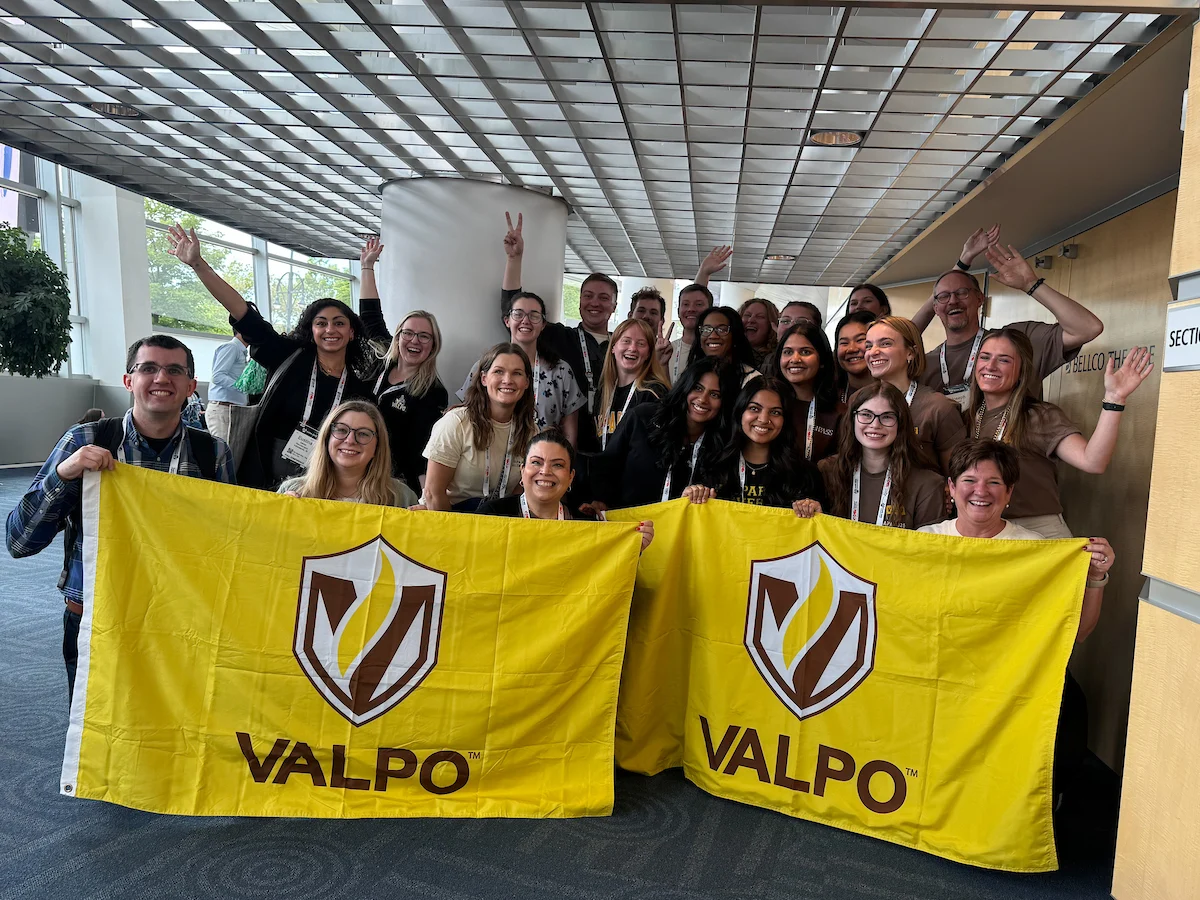 A group of people smiling and holding two yellow Valpo flags indoors, celebrating Alumni Success.