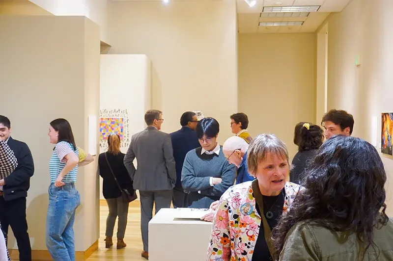 People mingle and view artwork at the brightly lit Brauer Museum of Art in Valparaiso, having conversations and looking at displays.