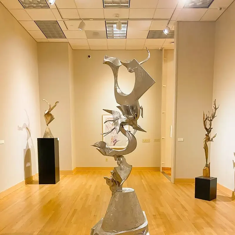 Abstract silver metal sculptures displayed in a well-lit art museum at Valparaiso, featuring wooden floors and beige walls, reminiscent of the exhibits at the Brauer Museum of Art.