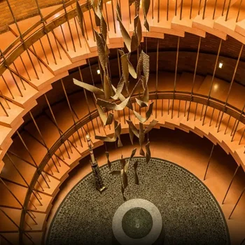 Spiral staircase with a hanging sculpture above a round stone floor and central circular fountain.