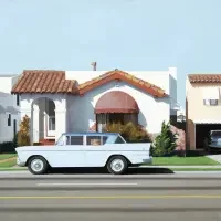 A vintage white car parked on a street in front of a house with a red-tiled roof, reminiscent of classic exhibitions & series celebrating timeless automotive design.