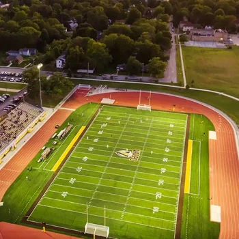Aerial view of an empty football stadium with a green field, track, and bleachers, surrounded by trees.