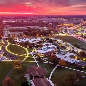 Aerial view of a campus at sunset with glowing walkways and vibrant pink and purple sky.