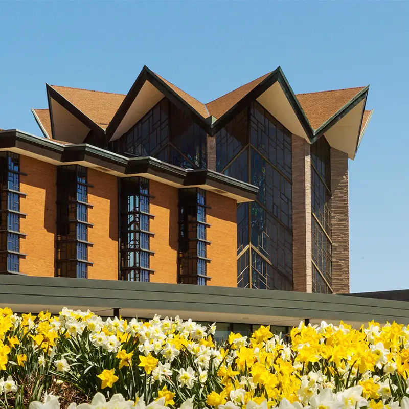 Modern brick and glass building with unique roof, behind a bed of blooming yellow and white flowers—captured perfectly for Valpo Digital Downloads.
