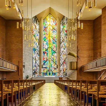 View of a church interior with wooden pews and a large colorful stained glass window at the front.