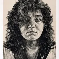 Black-and-white portrait of a person with wavy, shoulder-length hair, looking directly at the camera—an evocative image from recent exhibitions & series.