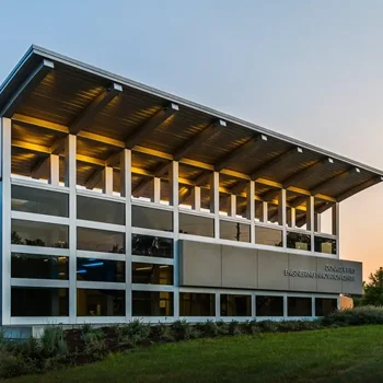 Modern two-story building with large windows and a slanted roof, lit warmly at sunset.